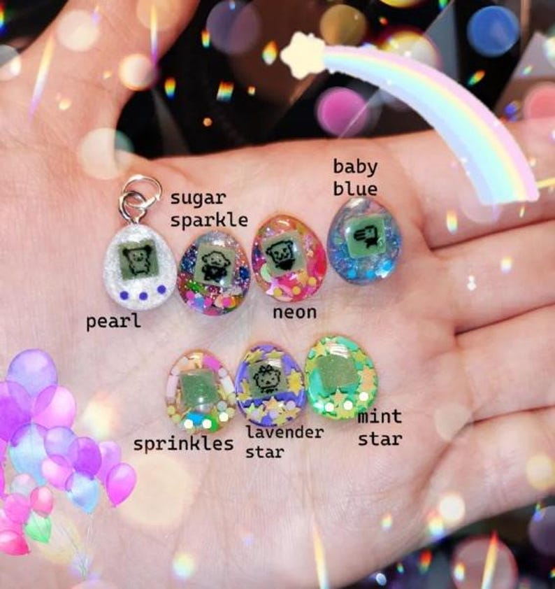May include: A collection of seven colorful, miniature, egg-shaped pendants. Each pendant features a small screen displaying a pixelated character. The pendants are labeled with names like "pearl," "sugar sparkle," and "baby blue."