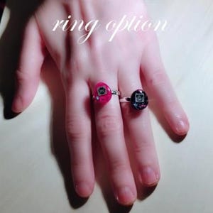 May include: Two rings with silver bands. One ring has a pink setting with a small graphic, and the other has a dark setting with a similar graphic. The text "ring option" is above the rings.