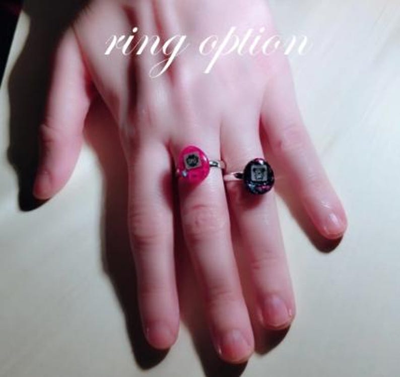 May include: Two rings with silver bands. One ring has a pink setting with a small graphic, and the other has a dark setting with a similar graphic. The text "ring option" is above the rings.