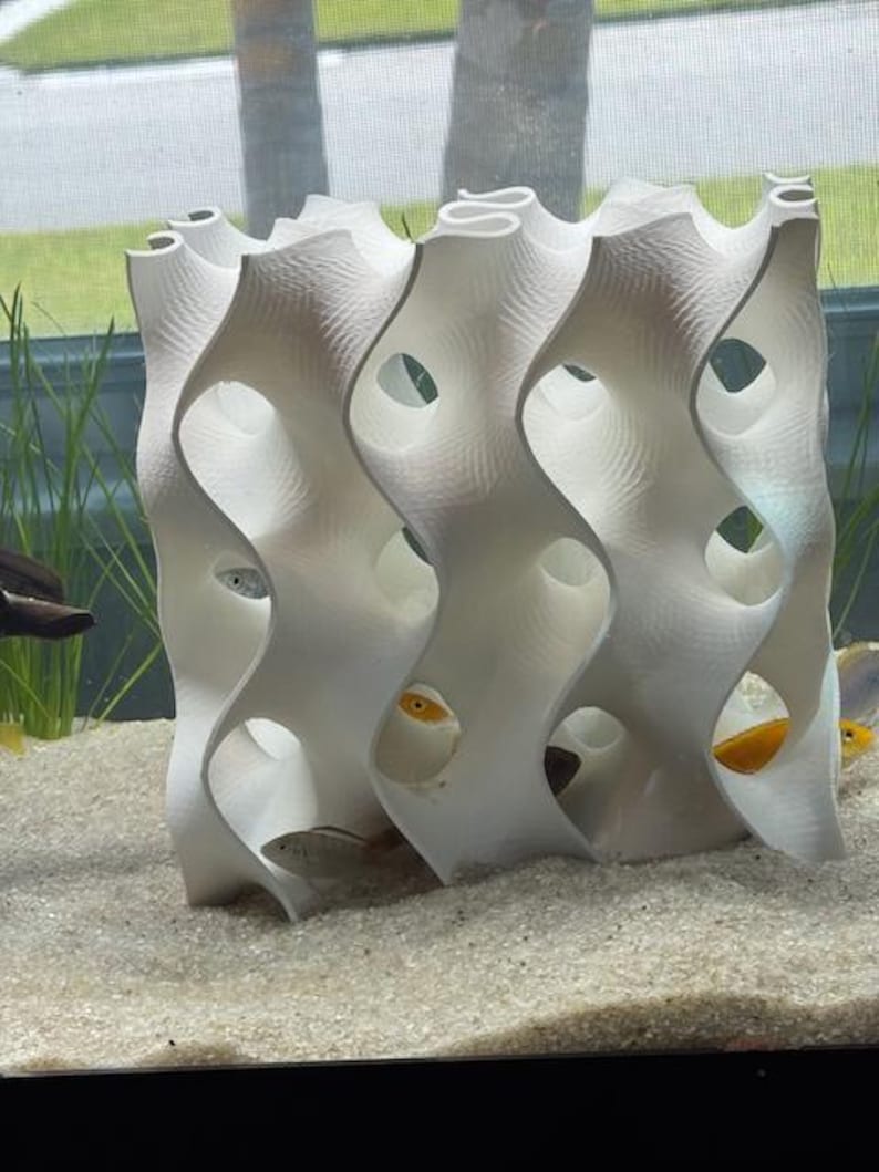 8x8 White 3D-printed gyroid aquarium cave in use, with fish hiding inside. The reef-safe design mimics coral structures, providing shelter and breeding spaces for cichlids, shrimp, and other pets. Enhances tank aesthetics and habitat.