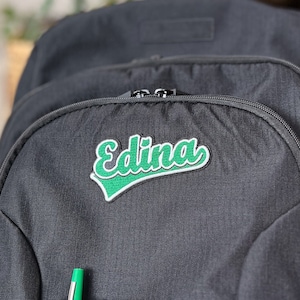 Puede incluir: Mochila negra con un parche bordado en verde que dice "Edina".