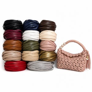 May include: A collection of twelve circular coils of flat leather cord in various colors including black, navy, brown, white, cream, olive, tan, red, and gray, alongside a light pink woven handbag with a pearl-accented handle and tassel.