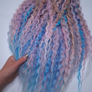 May include: A long, curly wig with blue, pink, and white streaks. The wig is styled in loose curls and has a soft, fluffy texture.