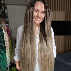 May include: A woman with long, straight, light brown hair styled in box braids. She is wearing a white button-down shirt.