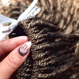 May include: Close-up of a bundle of brown and blonde synthetic hair extensions. The hair is in a twisted braid style. The hair is labelled "made with love" and "Boho crochet wave".