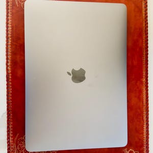 May include: A red leather laptop case with a decorative floral design. The case has a stitched border and a cutout for a laptop.