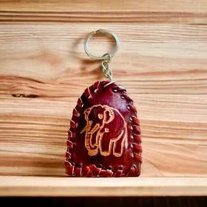 May include: A brown leather keychain with a stitched border and an elephant design. The keychain has a silver metal ring and chain.