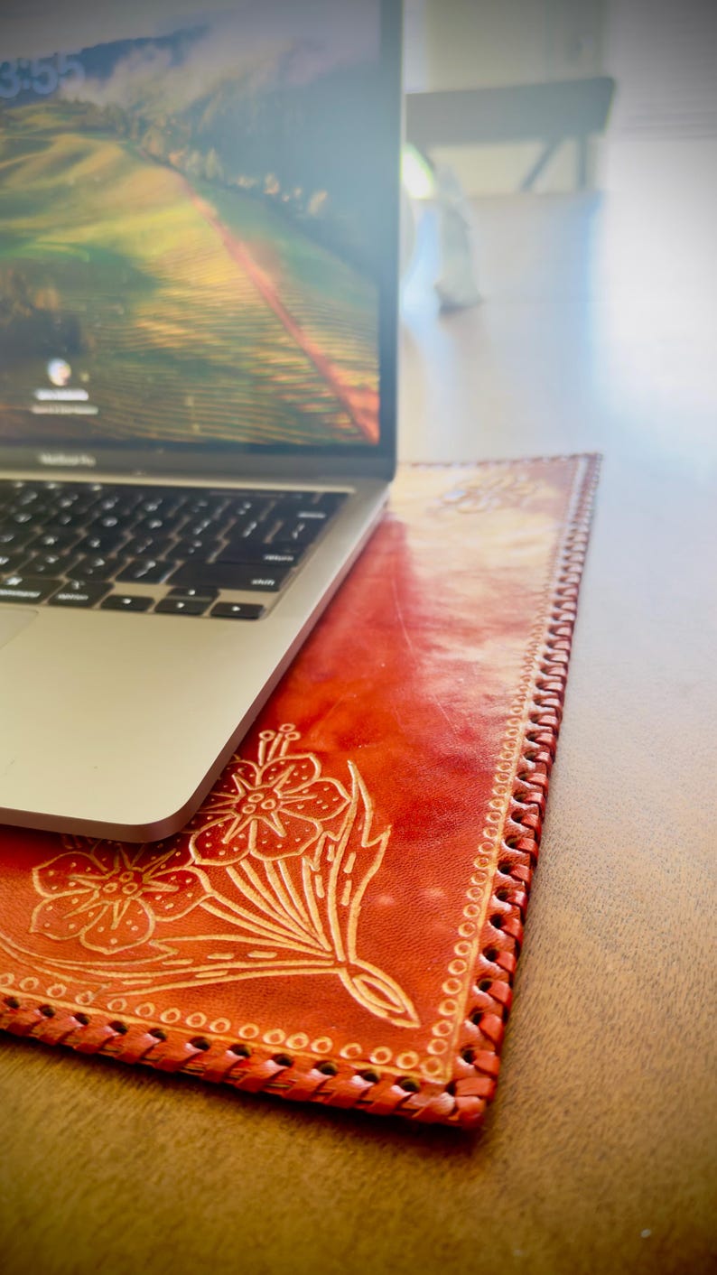 May include: A red leather laptop desk pad with a floral design. The pad has a stitched edge and is made of genuine leather.