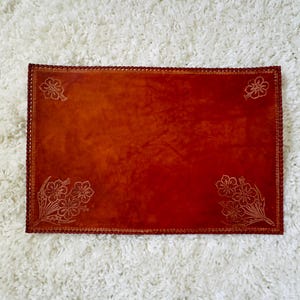 May include: A red velvet placemat with a decorative floral design. The placemat has a scalloped edge and is made of a soft, luxurious material.
