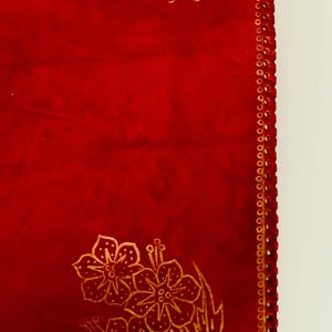 May include: Red leather journal with a gold floral design and a decorative stitched border.