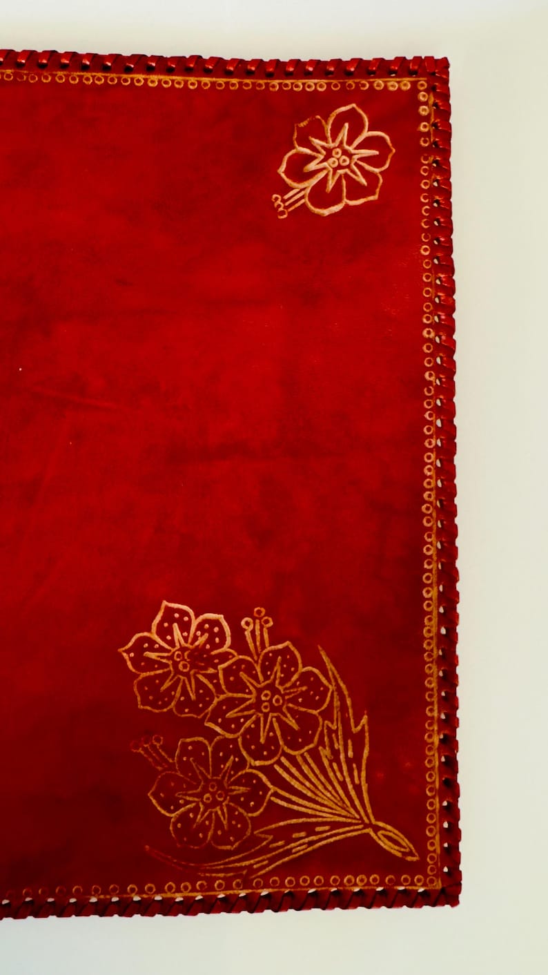May include: Red leather journal with a gold floral design and a decorative stitched border.