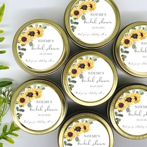 May include: Set of eight gold metal tins with white labels featuring a watercolor design of sunflowers and eucalyptus leaves. The labels include the text "NOEMI'S bridal shower 10-15-2022 thank you for celebrating with us".