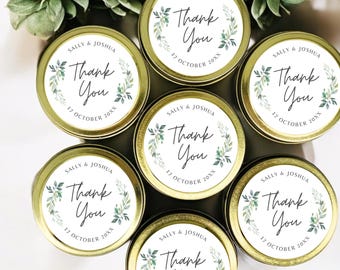 May include: A collection of small, round, gold-colored tins with white labels. Each label features the words "Thank You" in elegant script, surrounded by green leaf accents. The date "17 October 20XX" and names are also printed on the labels.