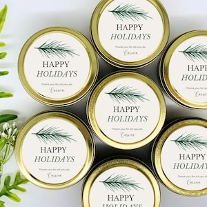May include: Six gold tins with white labels and green pine branch designs. Each tin has the text "Happy Holidays" and "Thank you for all you do, Carina".