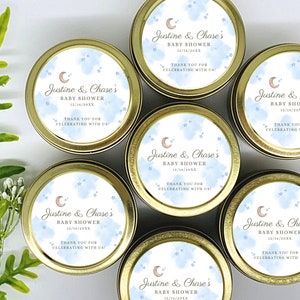 May include: Six gold favor tins with blue and white watercolor designs featuring a crescent moon and stars. Each tin has a label that reads "Justine & Chase's Baby Shower" with a date and the text "Thank you for celebrating with us!"