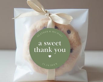 May include: A chocolate chip cookie in a clear cellophane bag, tied with a cream-colored ribbon. A green circular sticker reads "a sweet thank you" with a heart and date.