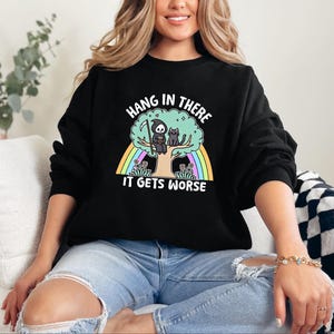 May include: Black sweatshirt with a graphic of a grim reaper and a cat sitting on a tree with a rainbow behind them. The text on the sweatshirt reads "Hang in there it gets worse".