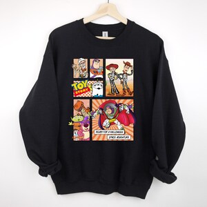 May include: Black sweatshirt featuring a comic-style graphic of Toy Story characters in Halloween costumes. The design includes Buzz Lightyear, Woody, and other characters. Text reads "Ready for a Halloween Space Adventure."