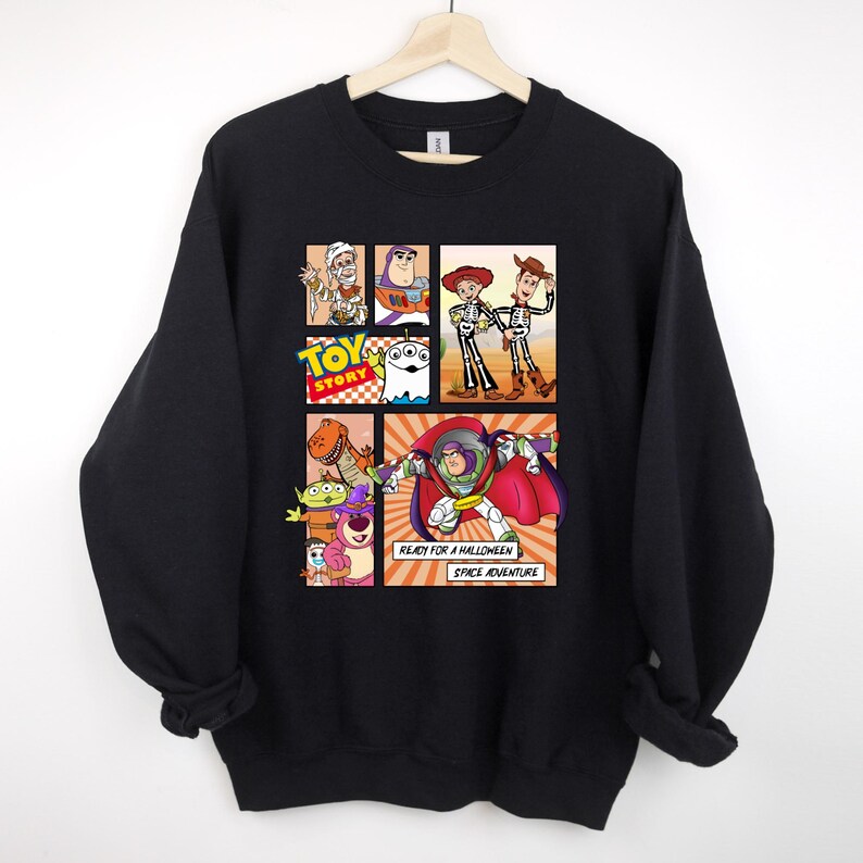 May include: Black sweatshirt featuring a comic-style graphic of Toy Story characters in Halloween costumes. The design includes Buzz Lightyear, Woody, and other characters. Text reads "Ready for a Halloween Space Adventure."
