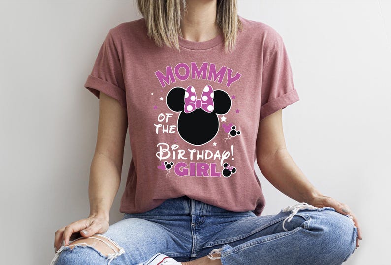 May include: A mauve t-shirt with the text "Mommy of the Birthday Girl" and a Minnie Mouse design. The design includes stars and Minnie Mouse icons. Ideal for a birthday celebration. The t-shirt is a relaxed fit.