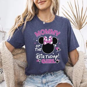 May include: A navy blue t-shirt with the text "MOMMY OF THE BIRTHDAY GIRL" in pink and white. The design includes a black Minnie Mouse head with a pink bow and stars.