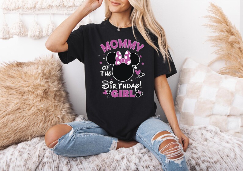 May include: Black t-shirt with the text "Mommy of the Birthday Girl!" in pink and white, featuring a Minnie Mouse design. The shirt has a round neck and short sleeves. The design includes stars and Minnie Mouse silhouettes.