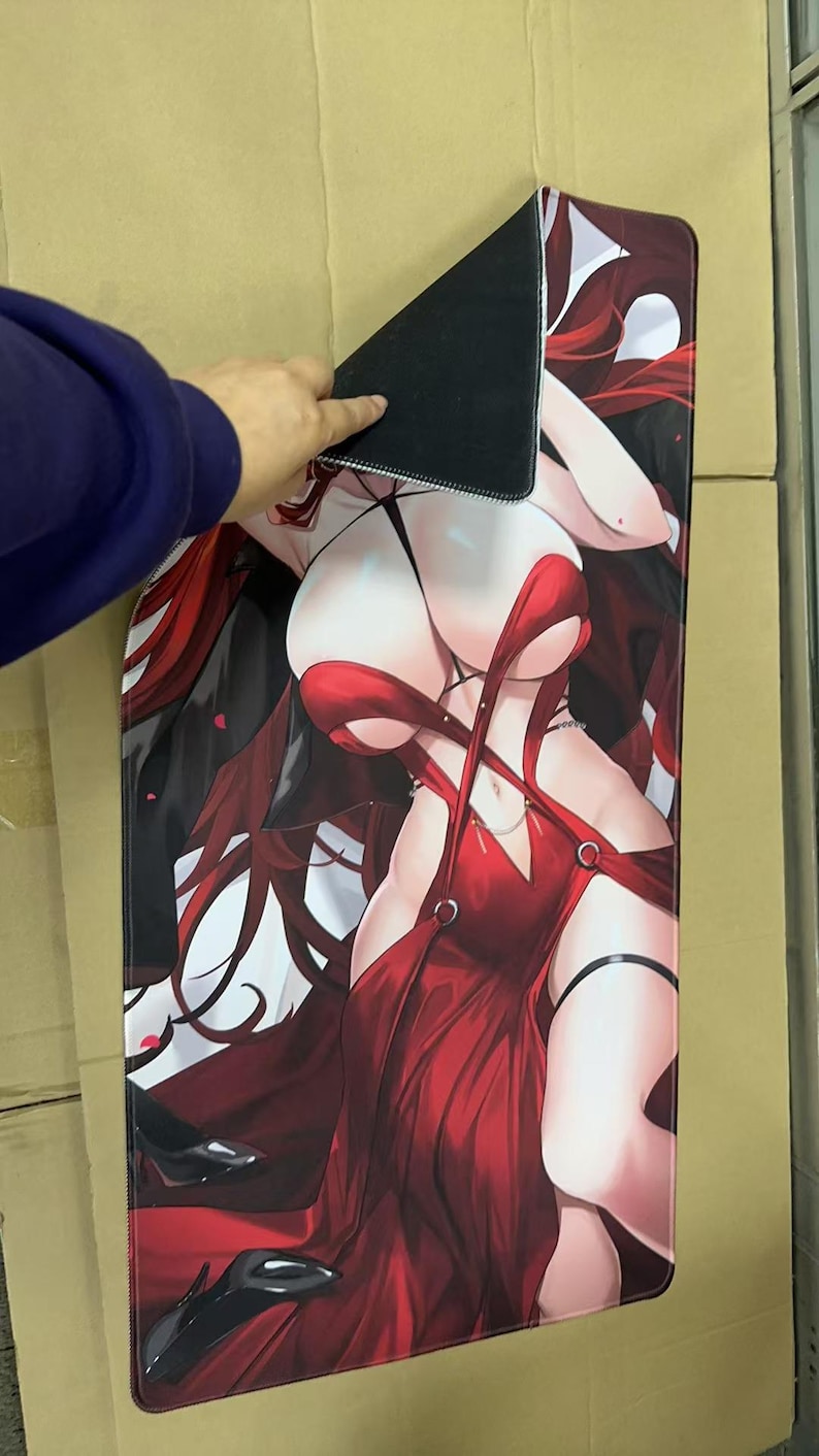 May include: A large rectangular mousepad featuring a stylized anime-style illustration of a woman in a red dress. The mousepad has a black backing and is being held up by a person's hand.