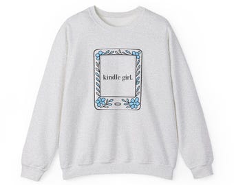 May include: A light gray heathered crewneck sweatshirt featuring a central graphic of a rectangular e-reader device outlined in black. The device is decorated with blue flowers and green leaves, and the text kindle girl. is printed in black.