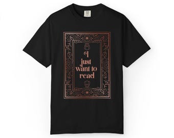 May include: A black short-sleeve t-shirt featuring a rose gold rectangular frame with intricate floral line art. Centered inside the frame is the text "I just want to read" in a matching rose gold serif font. The shirt has a crew neckline.