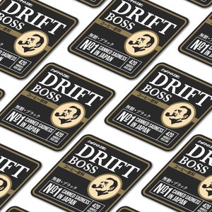 May include: A black and gold square sticker with the text "Drift Boss" in white. The sticker features a cartoon illustration of a man with a pipe and the text "No. 1 Canned Sadness in Japan".