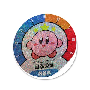 May include: A pink and white sticker with a cartoon character, a silver background, and a rainbow colored gauge with numbers 1 through 9. The text "NATURALLY ASPIRATED 自然吸気 装着車" is printed on the sticker.