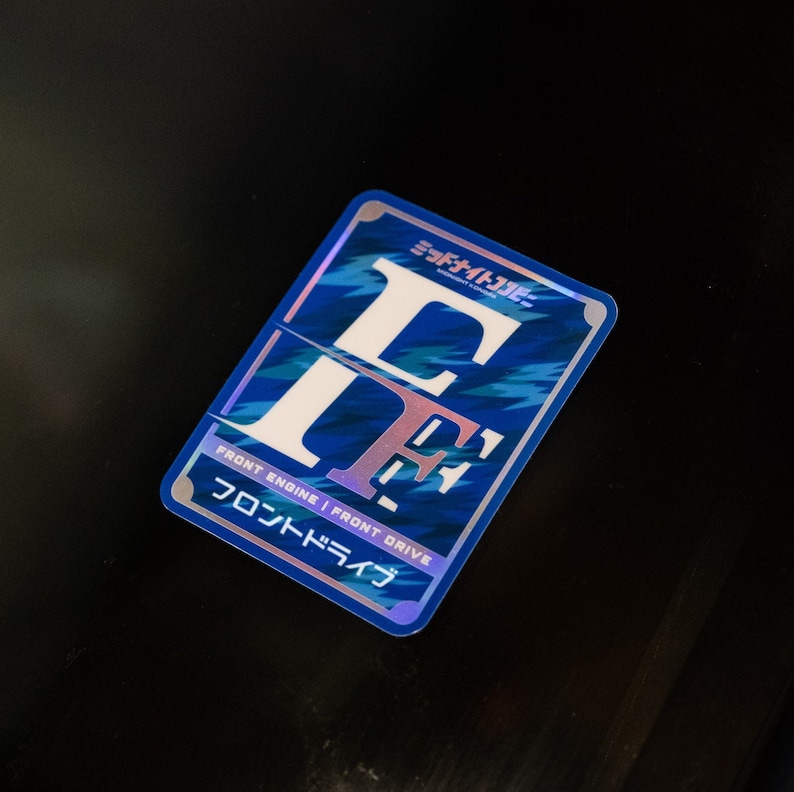 Op de afbeelding: Een blauwe en witte sticker met de letters "FF" in een gestileerd lettertype. De sticker zegt "Front Engine | Front Drive" en "フロントドライブ" in het Japans.