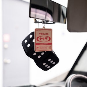 May include: A black and white dice car air freshener with a brown cardboard hanging tag that says "Yakuza" in English and Japanese. The tag also has a red circle with the Japanese word "Yakuza" in white text.