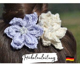 Puede incluir: Dos pinzas para el pelo de flores de ganchillo en morado y blanco con detalles de perlas. Las pinzas se llevan en el pelo de una mujer. El texto "Häkelanleitung" es visible en la imagen.