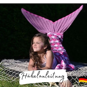 May include: A young girl wearing a pink and white crocheted mermaid tail. The tail is a blanket or a costume. The girl is sitting on a white net. The text "Häkelanleitung" is visible in the image.