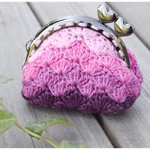 May include: A crocheted coin purse with a pink and purple ombre design. The purse has a silver metal clasp with two heart-shaped pieces.
