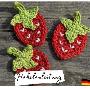 Peut inclure: Trois décorations en forme de fraises crochetées avec des feuilles vertes et des points blancs. Les fraises sont rouges et les feuilles sont vertes. Le texte "Häkelanleitung" est visible sur l'image.