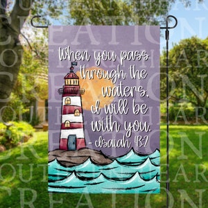 May include: A purple garden flag with a lighthouse, waves, and a sun. The text on the flag reads "When you pass through the waters, I will be with you. - Isaiah 43:2"