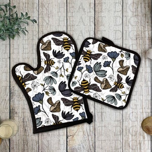 May include: A set of two oven mitts with a white background and a black and yellow bee and flower pattern. The mitts are made of a heat-resistant material and are perfect for protecting your hands while cooking.