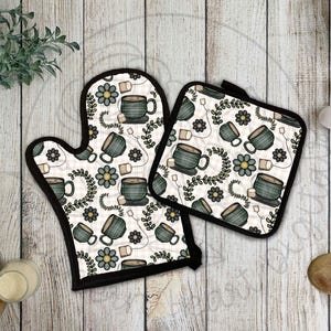 May include: A set of two oven mitts with a black trim and a white background. The mitts feature a repeating pattern of teacups, tea bags, and floral sprigs in shades of green and brown.