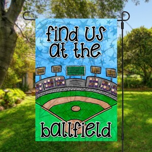 May include: A blue and green yard sign with white text that reads "Find us at the ballfield". The sign features a cartoon baseball field with bleachers and lights.