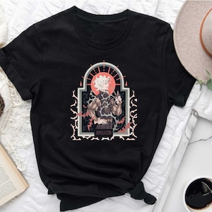 May include: Black t-shirt with a graphic print of a person with white hair standing in a gothic archway. The graphic has a red and white color scheme and the text "ASPHODEL" is printed below the person.