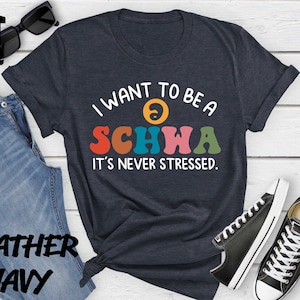 May include: A navy blue t-shirt with the text "I want to be a schwa it's never stressed." in colorful letters. The shirt has a yin-yang symbol above the text.