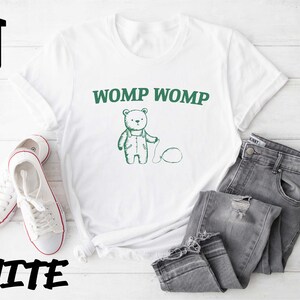 May include: White t-shirt with a green cartoon bear and the text "WOMP WOMP" printed on the front.