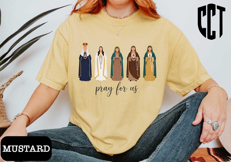 A person wearing a yellow t-shirt with a graphic design of five religious figures and the text "Pray for us" printed on it.