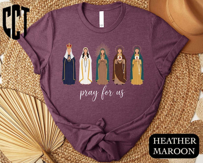 a purple t-shirt with a graphic design of five religious figures, including Mary, the Virgin Mary, and other saints, along with the text " Prayer for us" printed on it.