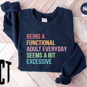 May include: Navy blue sweatshirt with the text "Being a Functional Adult Everyday Seems a Bit Excessive" printed in rainbow colors.