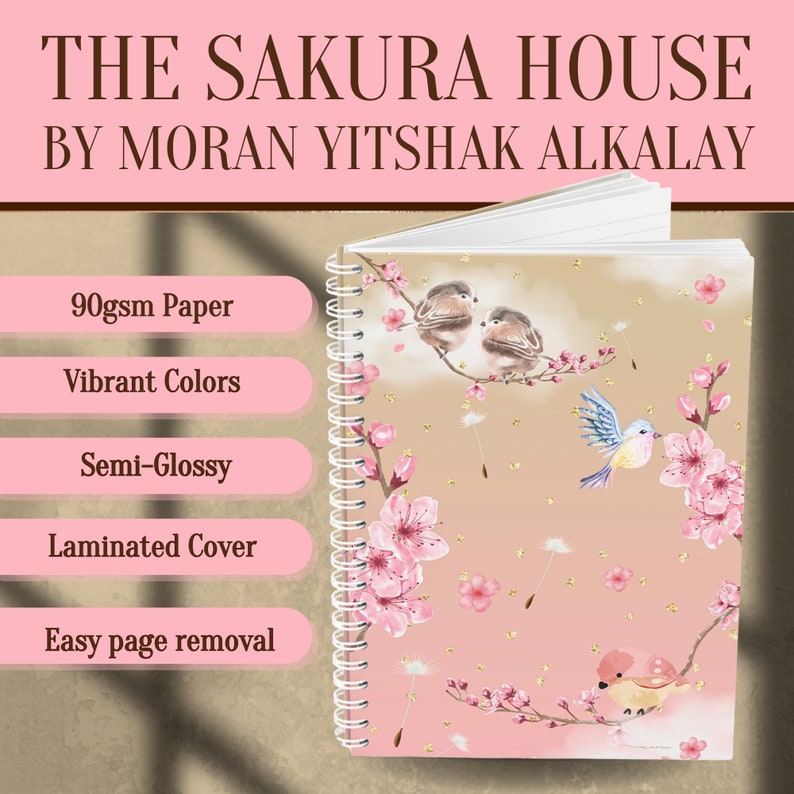 May include: A pink spiral bound notebook with a laminated cover featuring a floral design with pink cherry blossoms and gold accents. The cover also features a design of birds on branches. The text "THE SAKURA HOUSE BY MORAN YITSHAK ALKALAY" is printed on the cover.