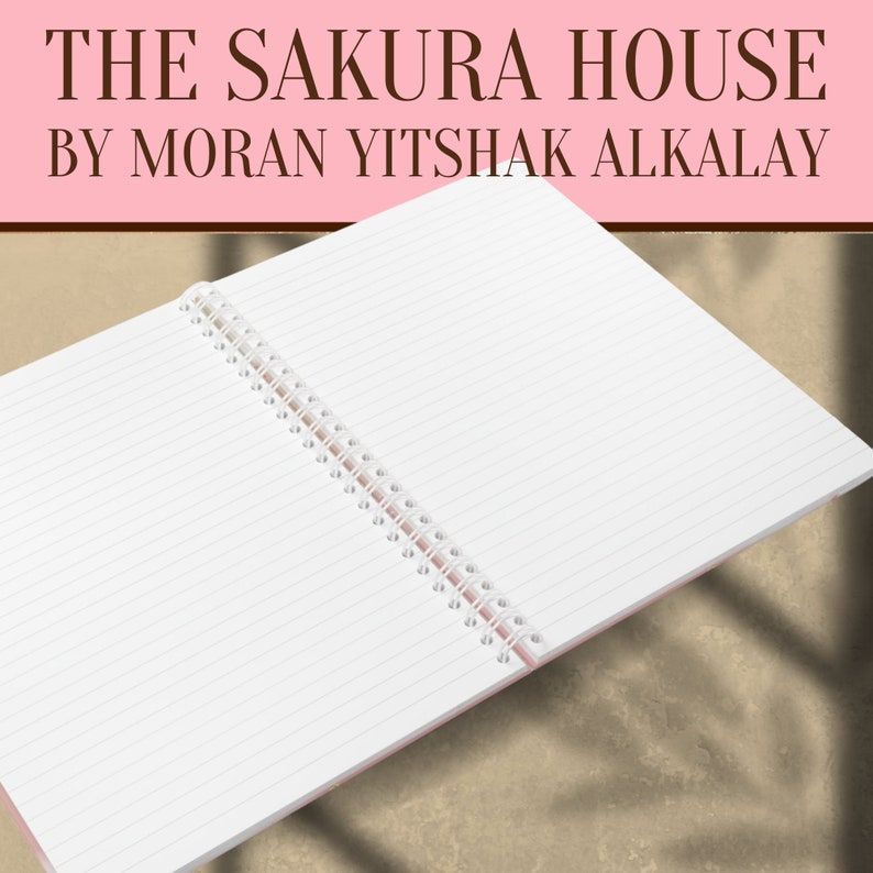 May include: An open spiral bound notebook with white lined pages and a pink cover. The notebook is lying open on a brown surface. The text "THE SAKURA HOUSE BY MORAN YITSHAK ALKALAY" is printed in black on a pink background at the top of the image.