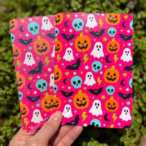 May include: Two rectangular notebooks featuring a vibrant hot pink background covered in a repeating pattern of orange jack-o'-lanterns, white ghosts, light blue skulls, black bats, yellow lightning bolts, and small stars.